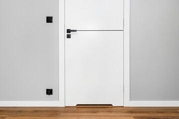 A white door with a ventilation undercut with a matte black handle and a black line in the middle in a modern house with vinyl panels on the floor.