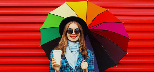Autumn portrait of happy smiling young woman with colorful umbrella wearing a checkered coat and beret on a white background