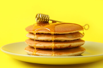 Plate of tasty pancakes with honey on color background