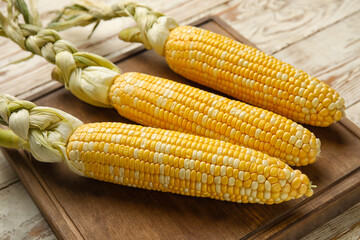 Board with fresh corn cobs on light wooden table