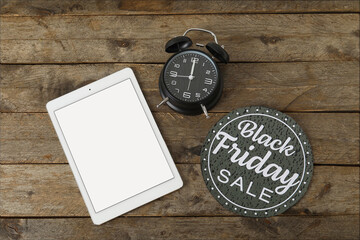 Tablet computer, alarm clock and card with text BLACK FRIDAY SALE on wooden background