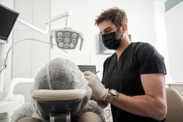 Odontólogo con barbijo, cura la boca de un paciente en su consultorio - obrazy, fototapety, plakaty