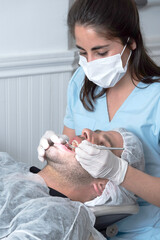 Mujer Odontóloga, revisa la boca abierta de un hombre en el consultorio con un espejo odontológico	