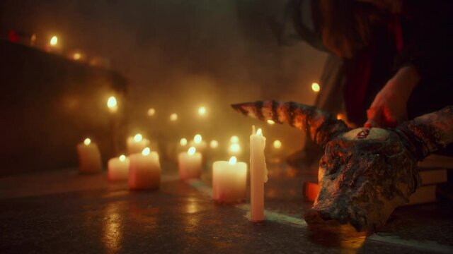 Crazy witch woman making fingerprint with blood on cow skull, sitting in pentagram circle. Evil sorceress doing rite and sacrifices at night, using black witchcraft, candles on floor. Halloween time.