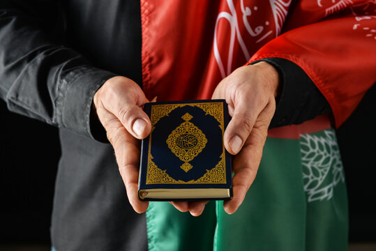 Man with flag of Afghanistan and Koran on dark background, closeup