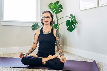 Woman sitting in yoga pose at home with eyes closed holding hands in mudra