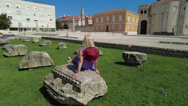 Woman with hat in the Ancient Roman Forum of Zadar city of Croatia on Adriatic Sea and capital of Dalmatia. Roman square with Church of St Donatus and Cathedral of St. Anastasia with the bell tower.