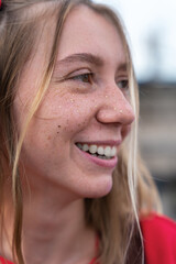 Vertical portrait of young smiling blonde woman with a soulful and playful look, freckles on her face, front view, close up.