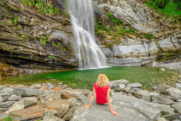 Woman sitting by the water of great waterfall of Bignasco, Valle Maggia, intersection point between the Bavona valley and Lavizzara valley, Cevio in Switzerland.