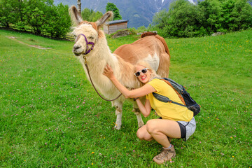 Backpacker woman taking a llama alpaca for a ride on top of Comino mount in Switzerland. Centovalli...