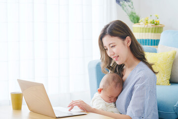 赤ちゃんを抱っこしてパソコンを使う母親