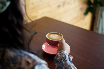 Selective focus shot of a coffee latte cup from above. An unrecognizable young woman holding coffee cup decorated professionally. 