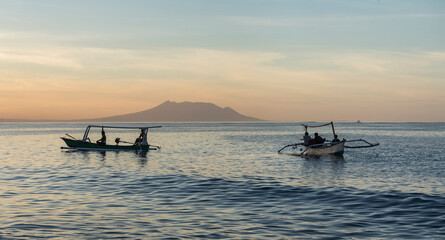 Local Balinese fishing boats along the shoreline in North Bali at sundown and facing a Java volcano nearby.