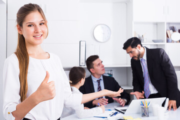 Fototapeta premium Confident smiling businesswoman with team in office showing thumbs up