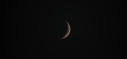 A wide dramatic night time closeup shot of a crescent moon with orange and yellow hues showing...
