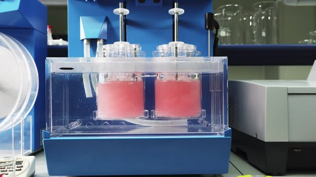 Working Dissolution Apparatus On The Table In The Pharmaceutical Laboratory. Zoom Out. Pink Liquid In The Containers. Modern Equipment For Chemical Analysis. Quality Control. Medicine Testing.
