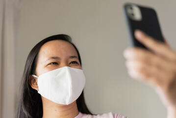 Asian woman with face mask using mobile phone for video calling
