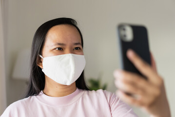 Asian woman with face mask using mobile phone for video calling
