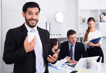 Portrait of happy businessman with working team behind at office