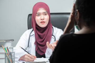 The Asian Muslim woman doctor was sitting at the patient's examination table and was examining and talking about the patient with a smiling and worried face.