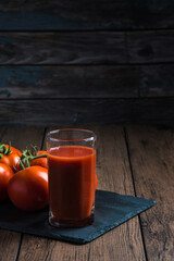 Tomato juice in a glass and a fresh tomato next to it on a wooden table