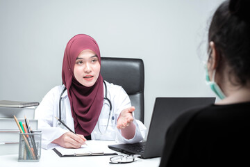 The Asian Muslim woman doctor was sitting at the patient's examination table and was examining and talking about the patient with a smiling and worried face.