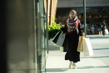 An Asian Muslim woman is carrying a bag of goods that she has been shopping for and buying a lot of products with happy, happy faces.