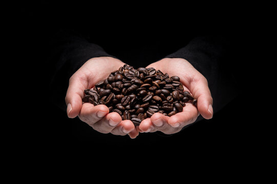 An image of a woman's hand holding a coffee bean with both hands until full, on black background.