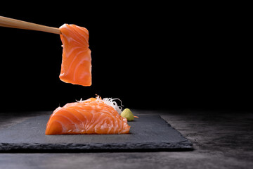 The hands were holding the chopsticks to hold the salmon sashimi, which was arranged on a black...