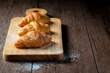 The newly baked croissant is placed on a wooden tray placed on a wooden table.