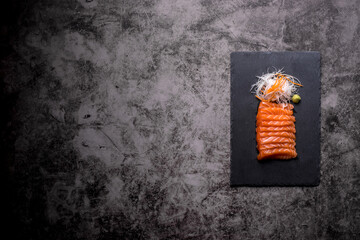 The salmon sashimi was laid out on a black stone plate on an old table, with copy space.