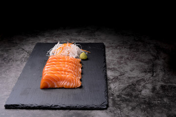 The salmon sashimi was laid out on a black stone plate on an old table, with copy space.