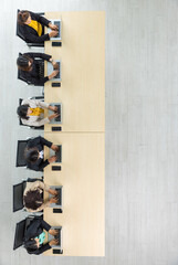 Table top view of six Asian business women sitting and working on laptops in straight line on wooden conference table in office. Concept for business meeting