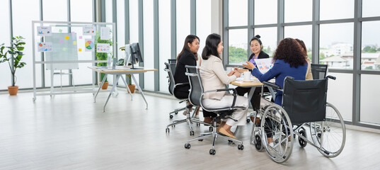 Asian business women and handicap woman sitting on wheelchair are in meeting together on the table...