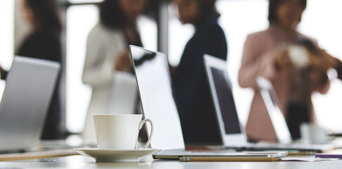 Selective focus on working desk, group of unrecognizable businesswomen standing together in office at breaking time. Female employee teamwork taking with relax in blur background