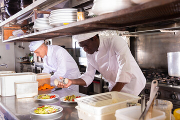 Portrait of confident experienced aframerican chef in white uniform working in professional kitchen...