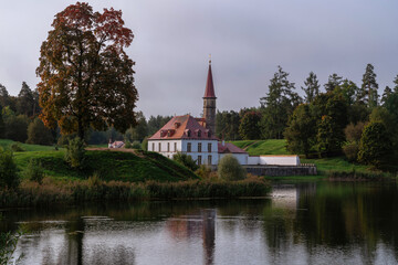 View of the Priory Palace on the shore of the Black Lake on an autumn sunny evening with clouds, Gatchina, St. Petersburg, Russia