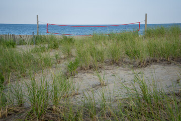 View from boardwalk overlooking grass and beach volleyball net, ocean in distance. 