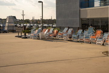 Stacked pool chairs, background against parking lot, concrete in foreground with copy space. 