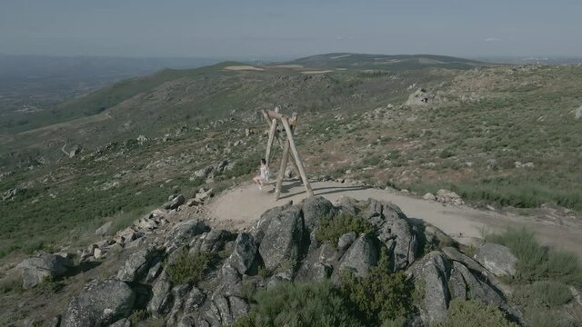 Woman swings on the top of a rocky hill overlooking a beautiful valley.