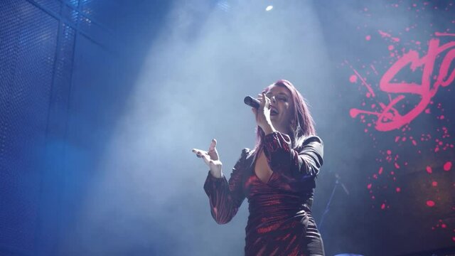 A smoke-filled nightclub or cabaret and a female performer singing into a cordless microphone and using hand gestures.