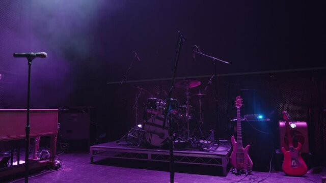 Cinematic footage of a stage set up ready for a rock band to perform. Guitars, drums, and microphones are ready for the performers. Purple lite stage. Handheld medium shot