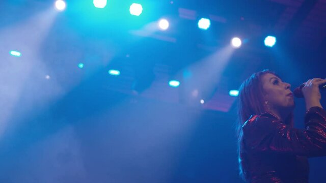 Close up of a female performer singing into a microphone with lots of stage lights shining on her.