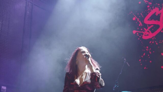 Handheld cinematic shot of a female performer singing into a microphone on stage and dancing.