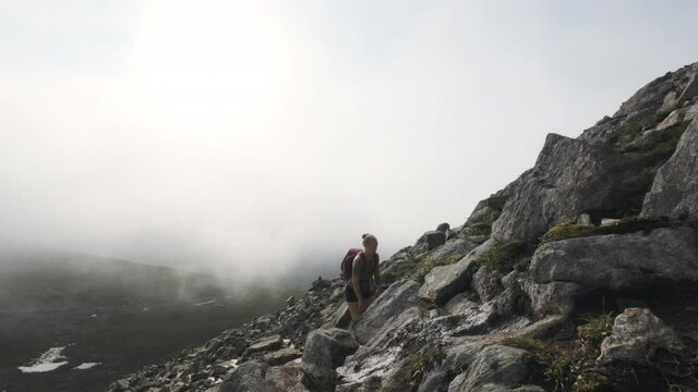 Woman Traveler With Backpack Hiking On Rocky Cliff On A Cloudy Day - slow motion