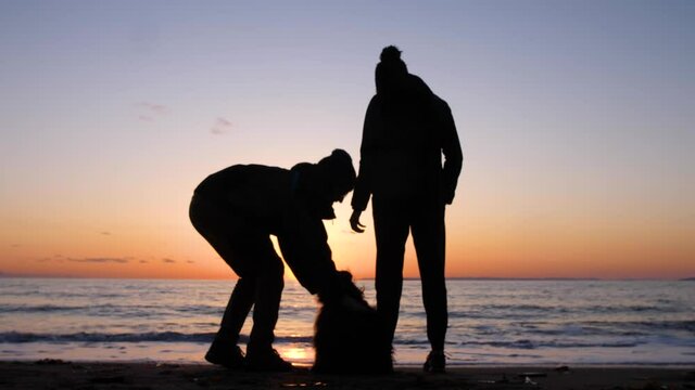 silhouette of couple and their playful dog at the beach