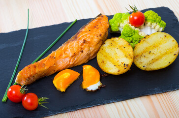 Grilled salmon served with potatoes, fried egg yolk, cherry tomatoes, broccoli and scallions on...