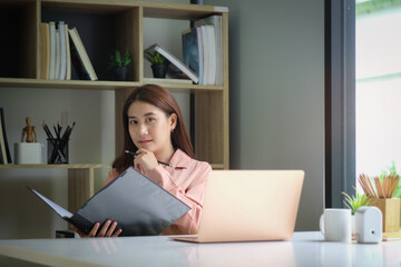 Portrait of happy young woman working on tablet pc while sitting at her working place in office..