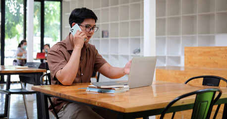 Smart Asian businessman talking on mobile phone and working with laptop computer.