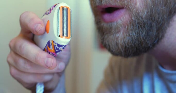 Little handheld electric razor being blown out by blonde honey bearded white caucasian man. In Cinema 4k (4096x2160) 30fps slowed from 60fps.